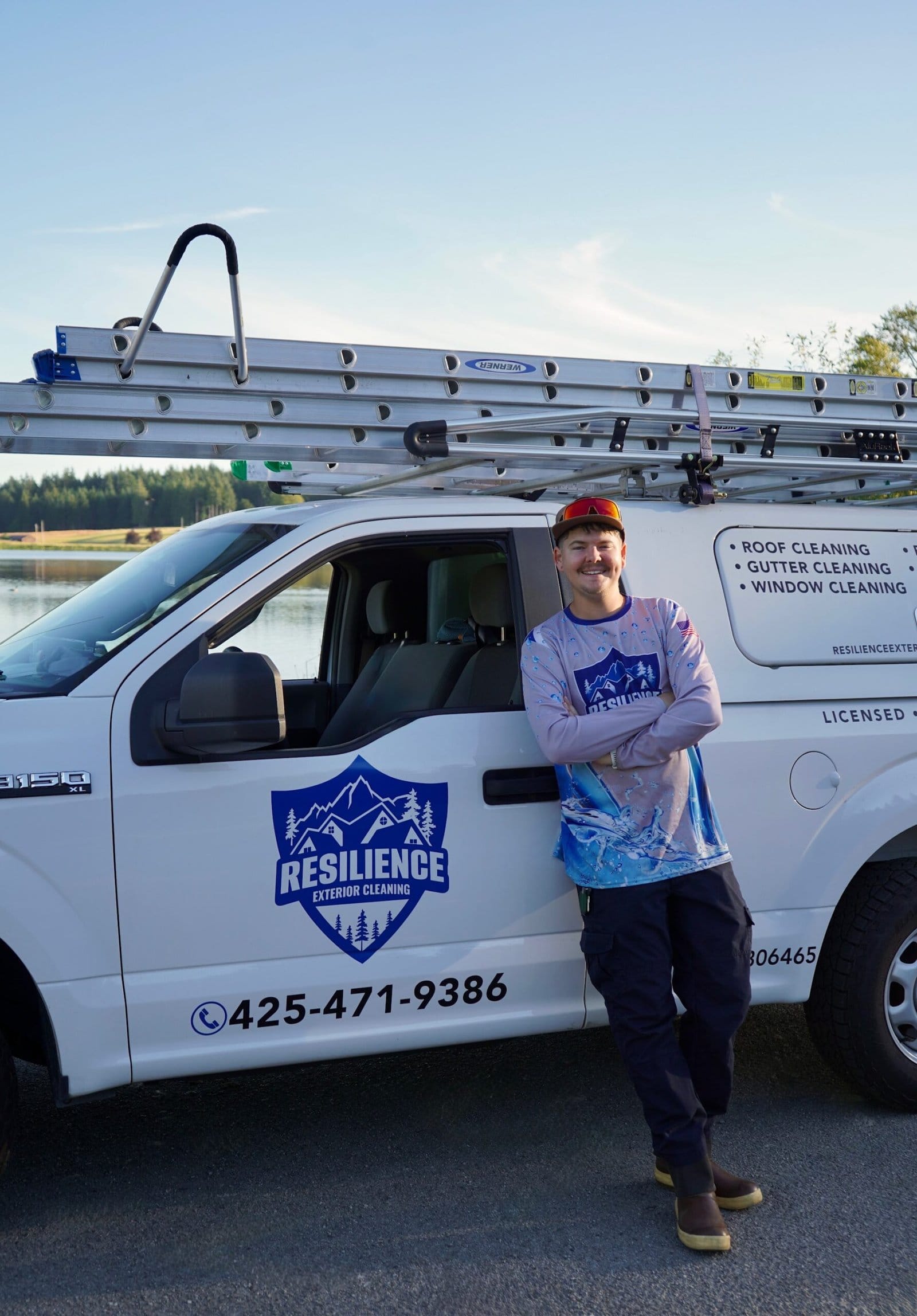 A Resilience Exterior Cleaning crew member standing beside the company's branded Ford F-150 with ladders racked, at a lake in Snohomish County.